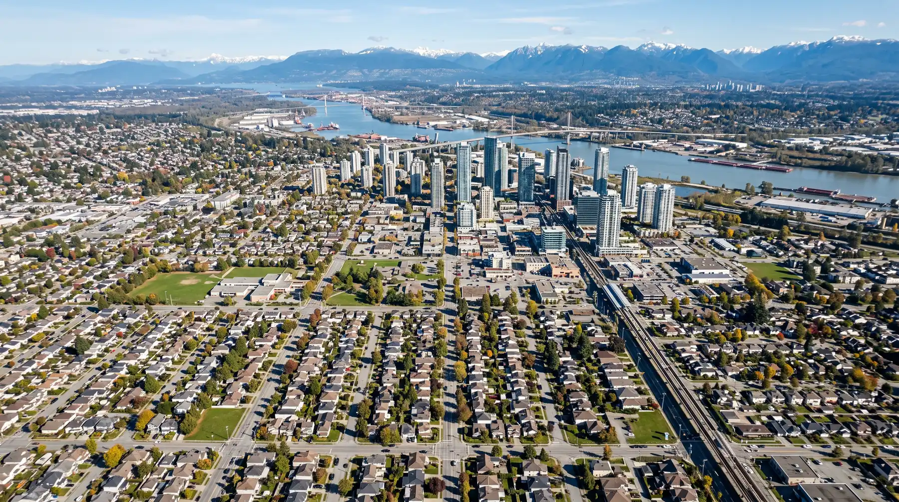 Aerial view over Surrey neighbourhoods and City Centre towards the Fraser River and mountains